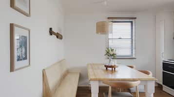 Een eethoek met een houten tafel en bank, een hanglamp en een raam met zonwering.