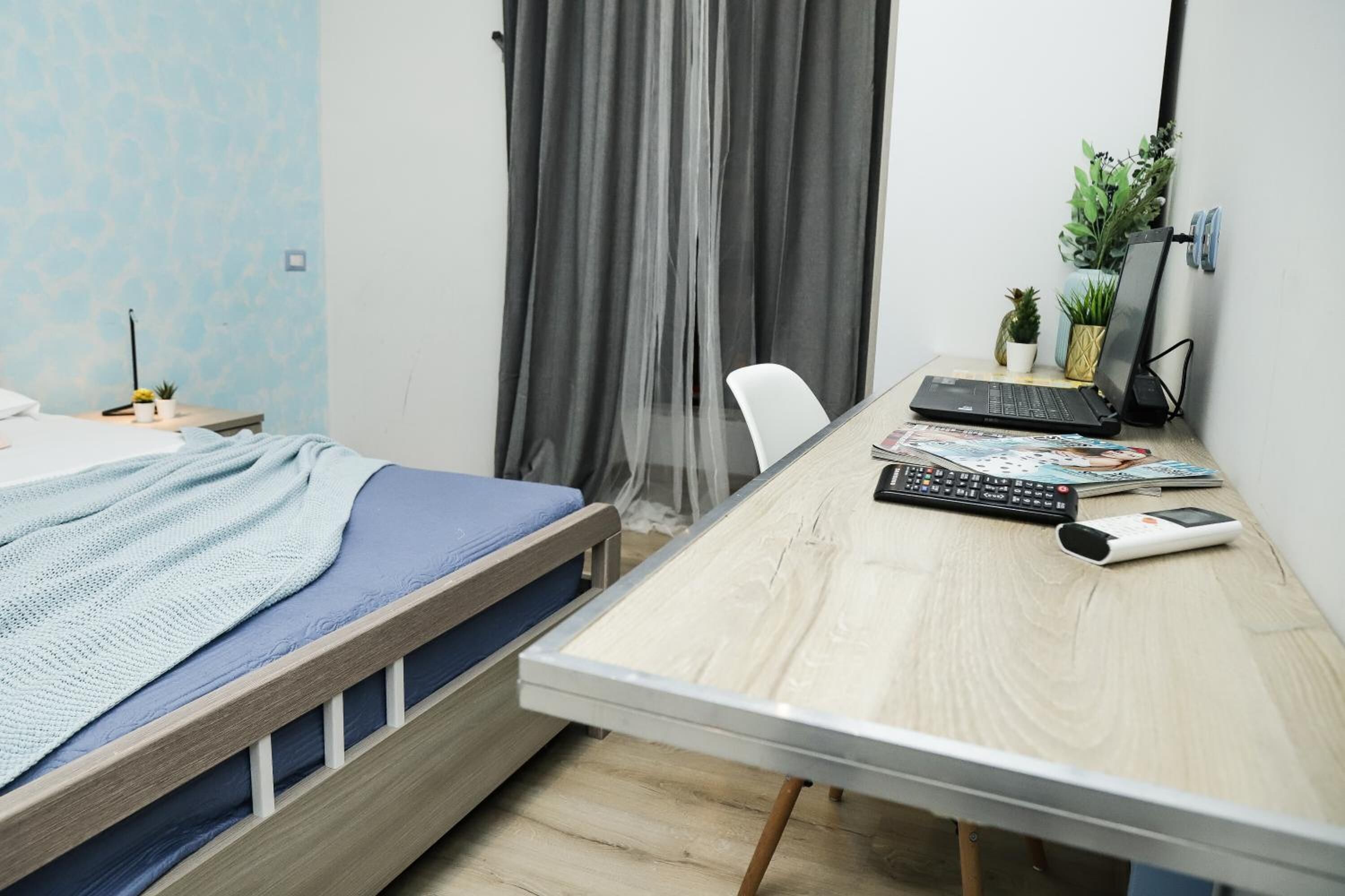 Una camera da letto con un letto, una scrivania, un portatile, una tastiera, un mouse e una piccola pianta in vaso.