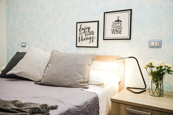 Una cama bien hecha con almohadas, una lámpara de noche y una cita enmarcada en la pared.