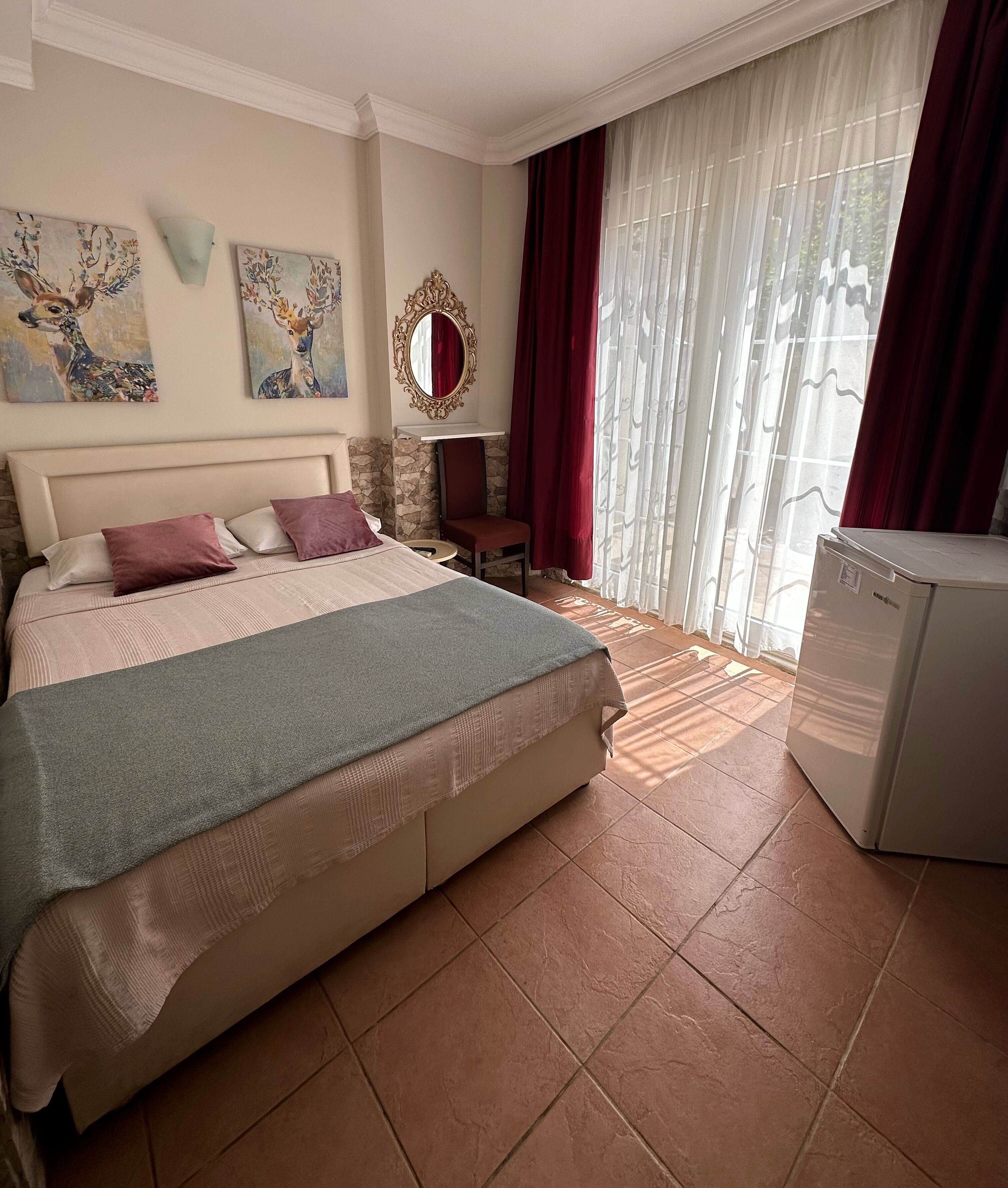 A hotel room with a bed, a small table, a chair, a mirror, and a refrigerator.
