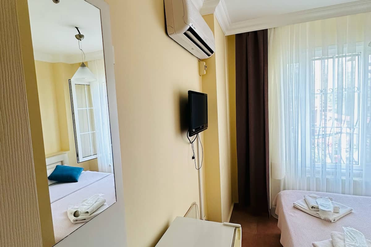 A hotel room with a bed, a small desk, a mirror, an air conditioning unit, and a window with curtains.