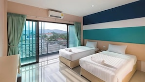 Habitación de hotel con dos camas, un ventanal con cortinas, equipo de aire acondicionado y vistas a la ciudad.