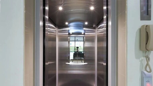 Un ascensor con puerta de vidrio, interior visible y un teléfono instalado en la pared.