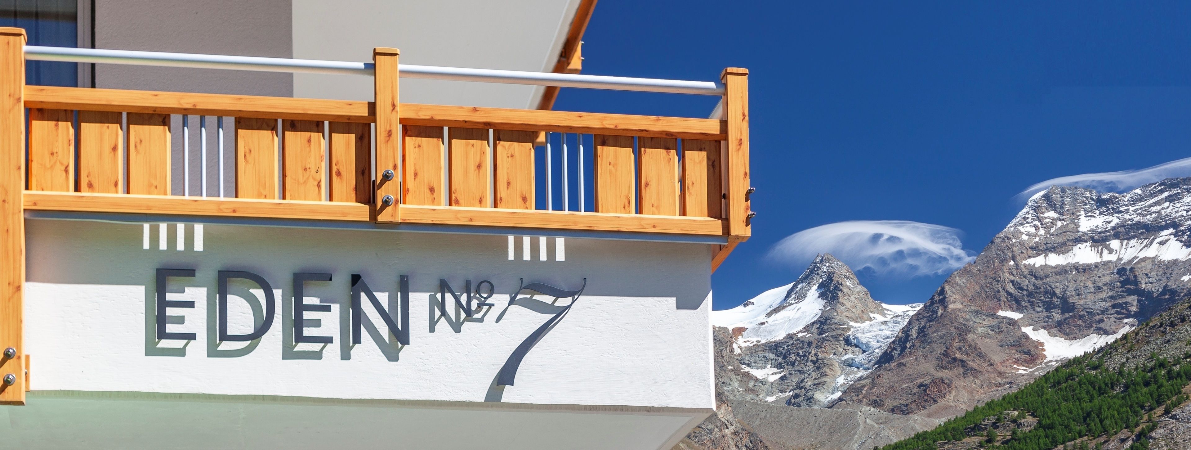 A wooden balcony with a sign reading "EDEN No.7" against a mountain backdrop.