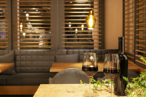A restaurant interior with a table set for two, featuring two wine glasses and a bottle. - Hotel Eden No. 7 (Saas-Fee)