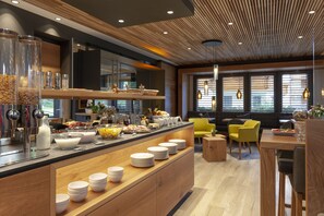 A modern kitchen with a wooden island, glass jars, and a dining area with yellow chairs and a wooden table. - Hotel Eden No. 7 (Saas-Fee)