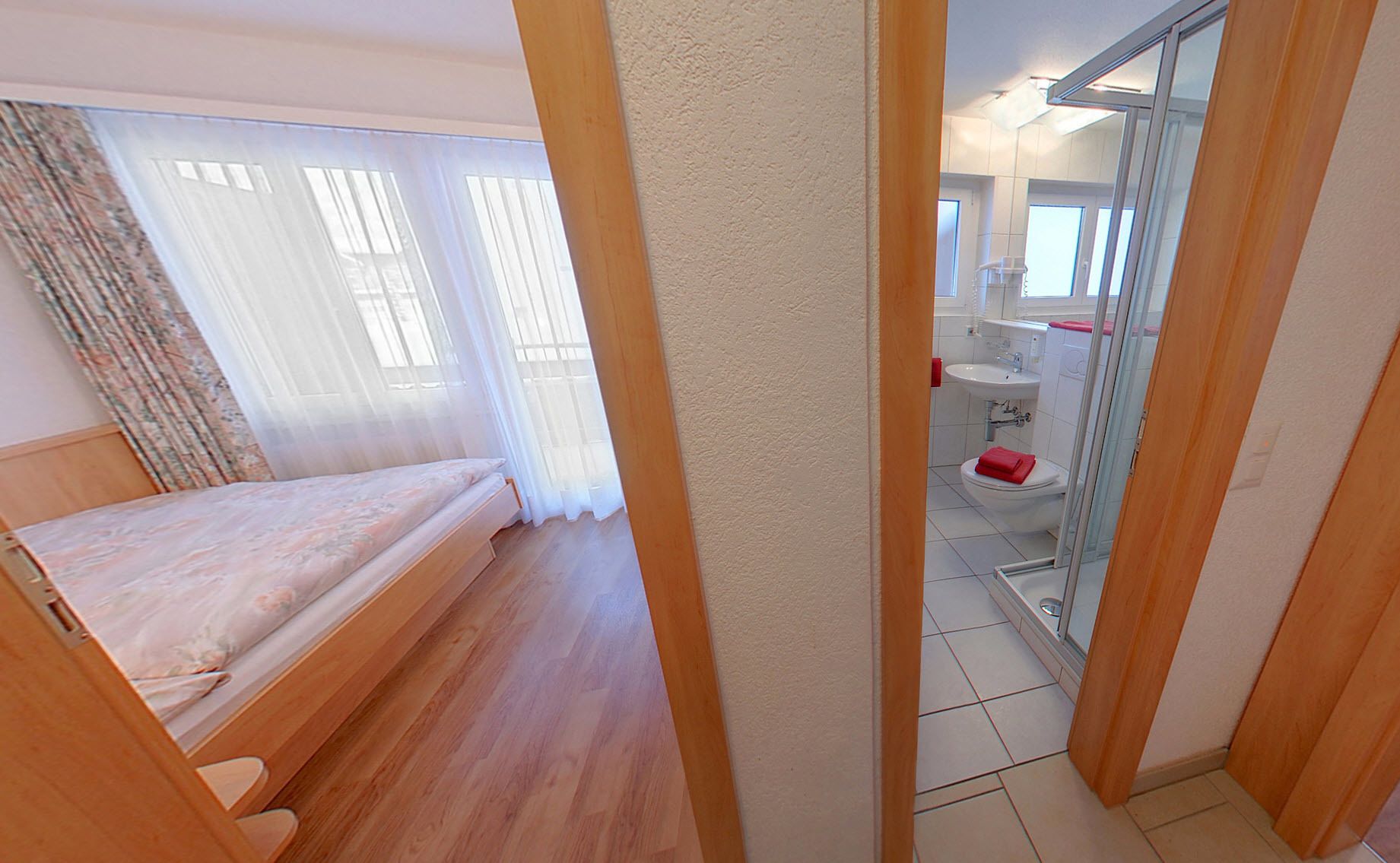 A bedroom with a wooden bed, a bathroom with a toilet and sink, and a glass shower door.