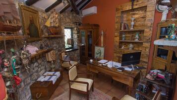 A rustic room with a wooden desk, a computer, and various decorative items including a ship model, a statue, and a framed portrait.