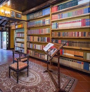 A library with wooden bookshelves filled with books, a reading stand, and a patterned rug. - Agriturismo Papyrus (Syracuse)