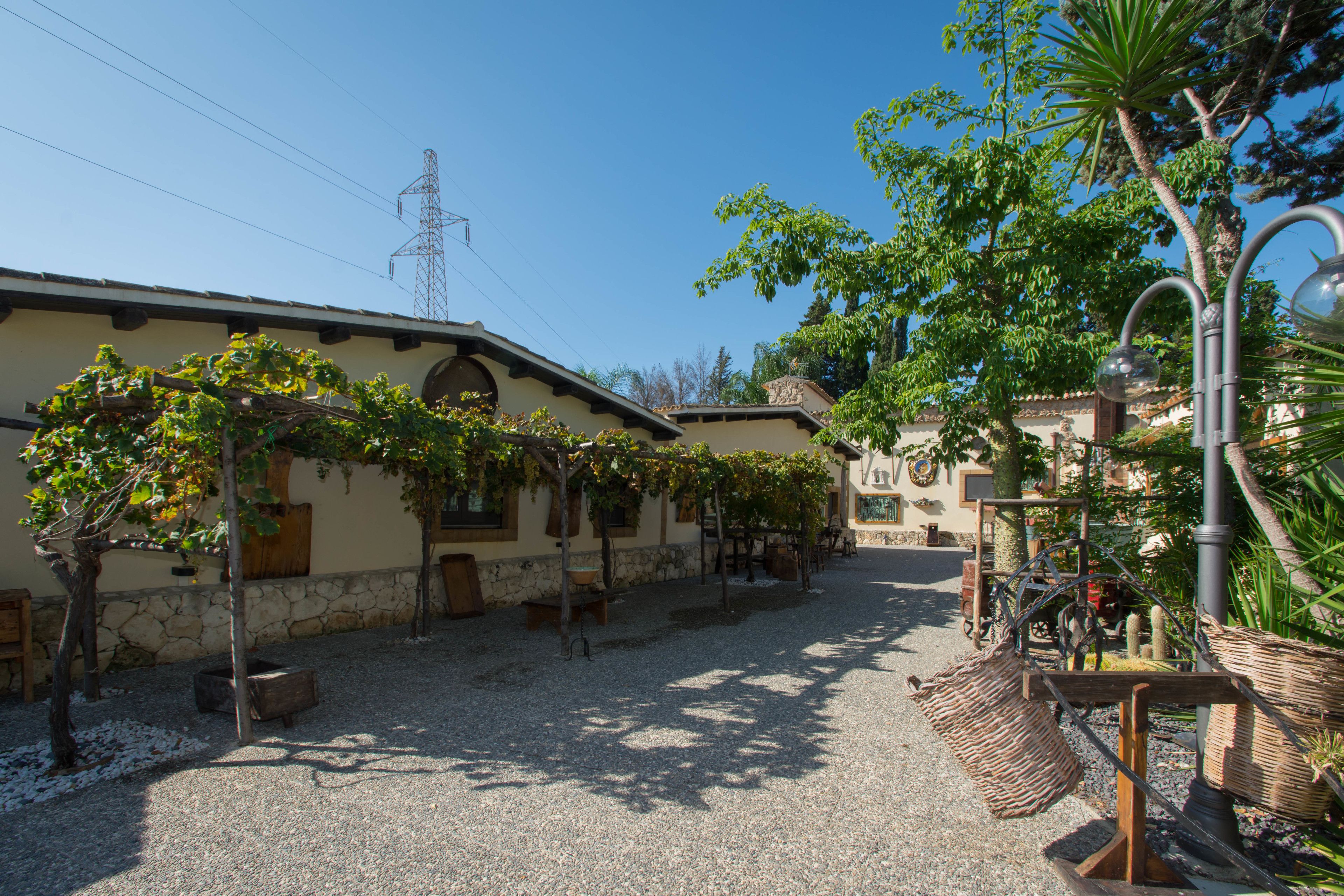 Une cour avec un chemin de gravier, un bâtiment doté d’un mur en pierre et une pergola couverte de plantes grimpantes.