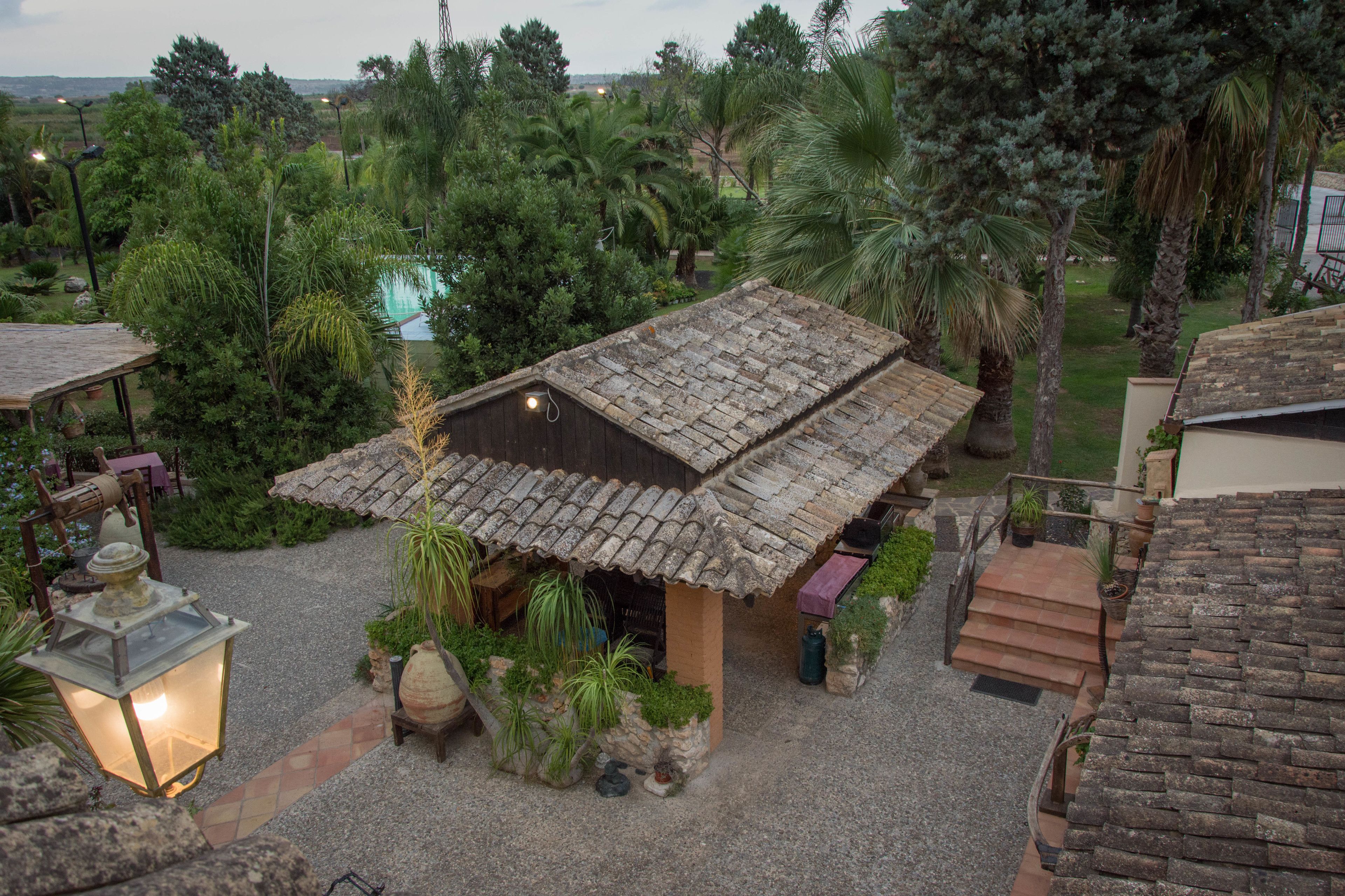 A rustic building with a tiled roof, surrounded by lush greenery and palm trees.