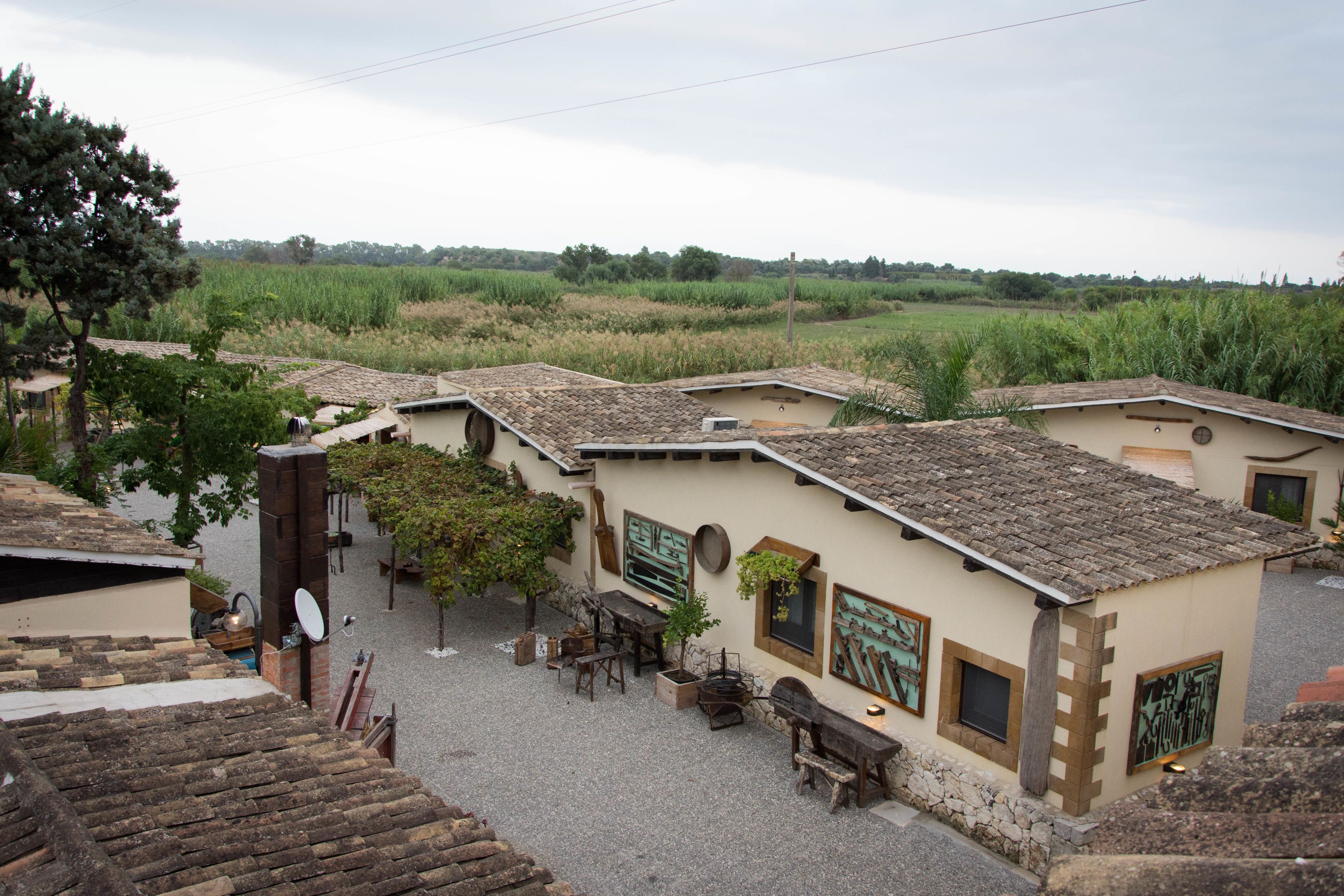A rustic building with a tiled roof, surrounded by a gravel courtyard, featuring outdoor seating and a small garden area.