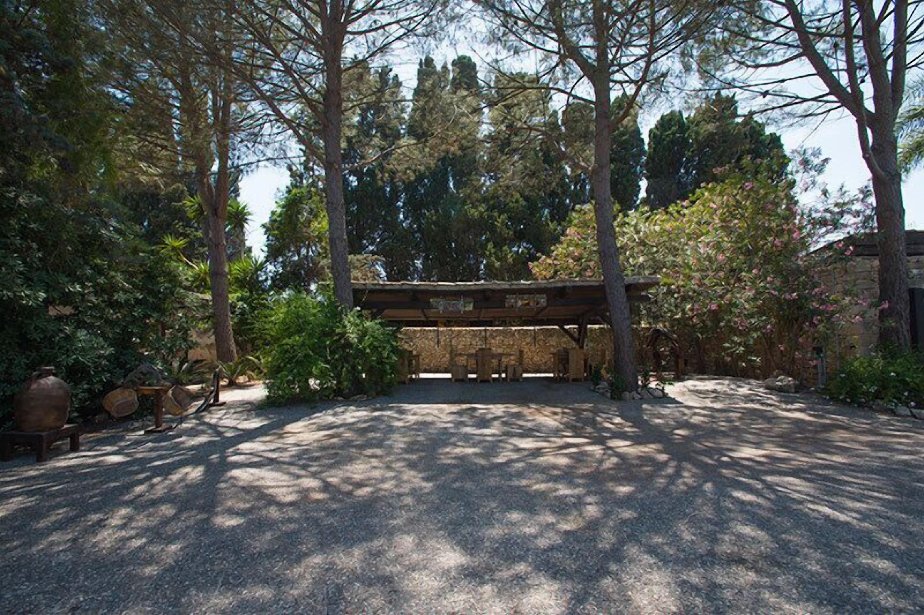 A covered outdoor area with a gravel path, surrounded by trees and a stone wall.