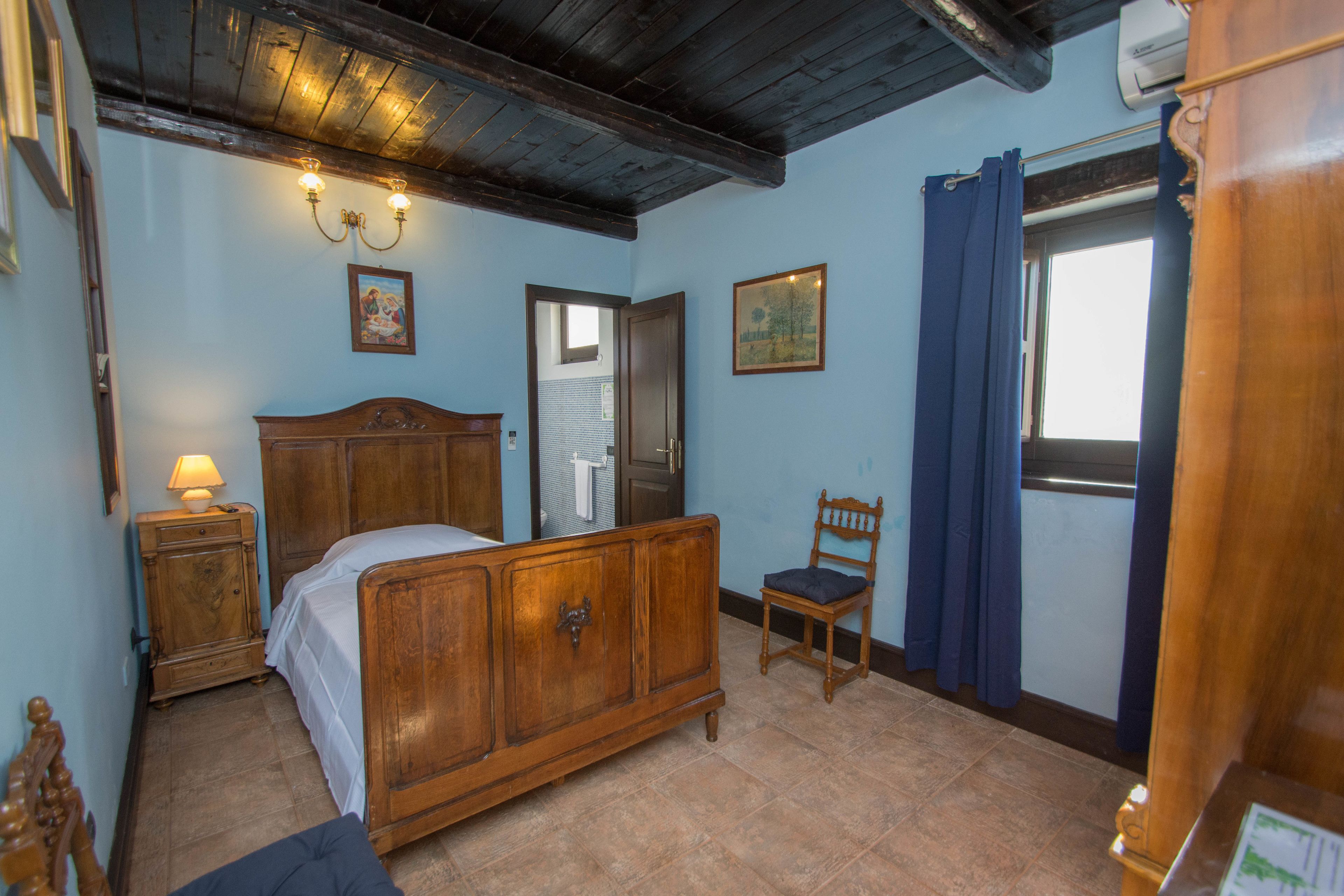 Ein Schlafzimmer mit einem hölzernen Bett, einem Nachttisch, einem Sessel und einem Fenster mit Vorhängen.