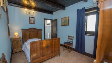 Ein Schlafzimmer mit einem hölzernen Bett, einem Nachttisch, einem Sessel und einem Fenster mit Vorhängen.
