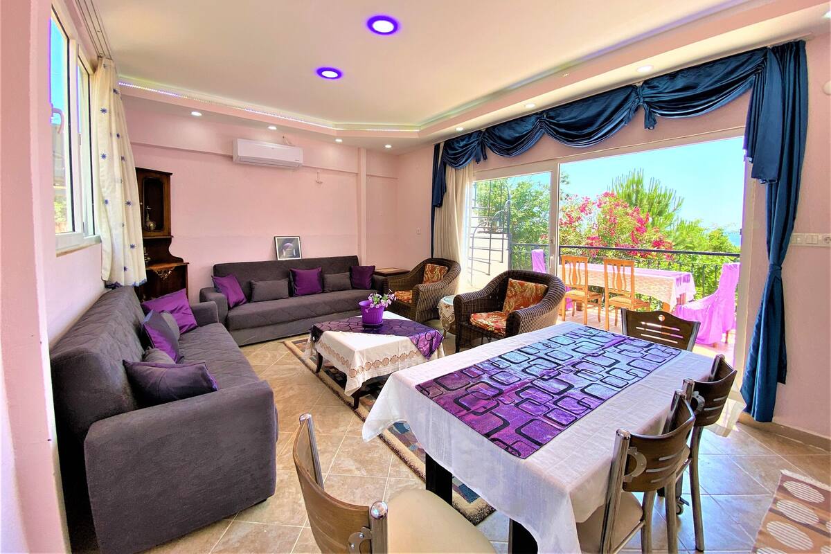 A spacious living room with a sofa, chairs, a dining table, and a balcony with a view.