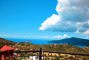 A balcony with a view of a coastal landscape, including a body of water and distant mountains.