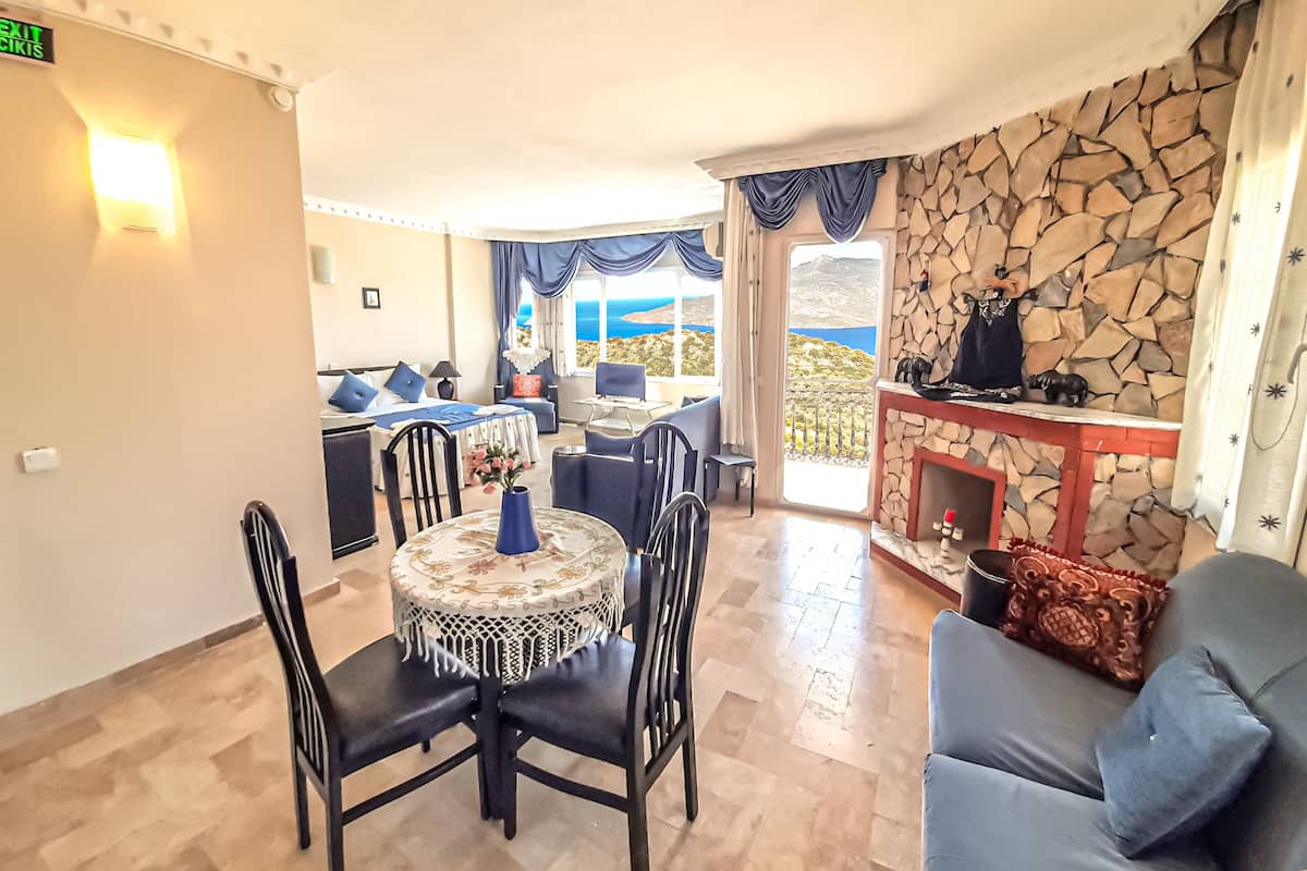 A hotel room with a dining area, a stone fireplace, and a view of the sea.