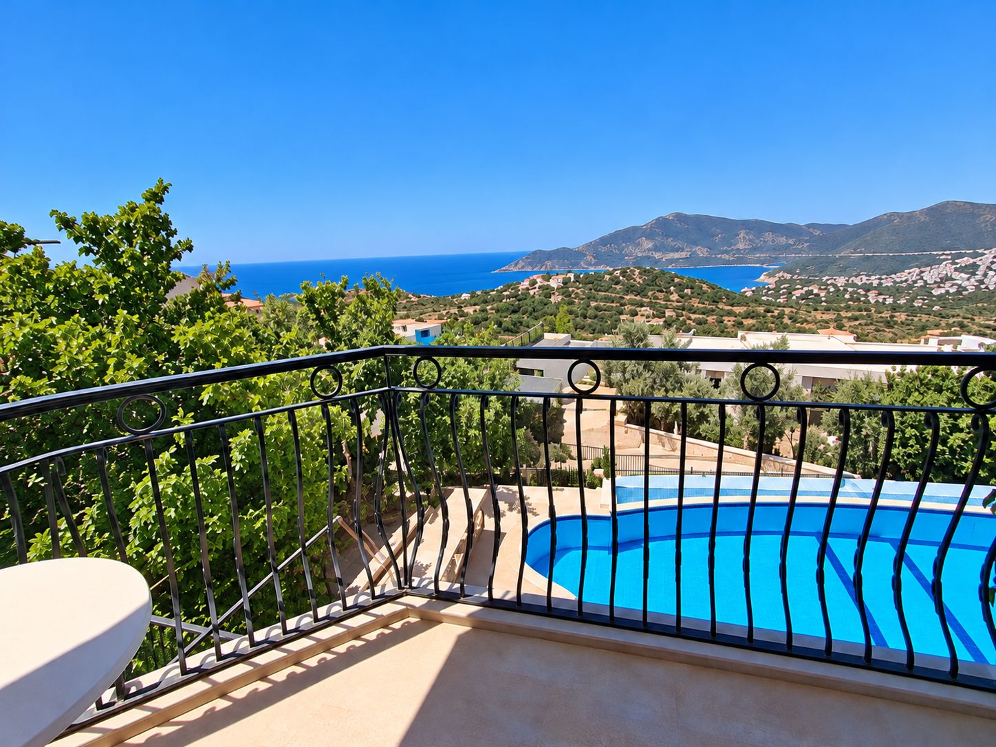 Un balcon avec une piscine, offrant une vue sur un paysage côtier avec des montagnes et un ciel bleu dégagé.
