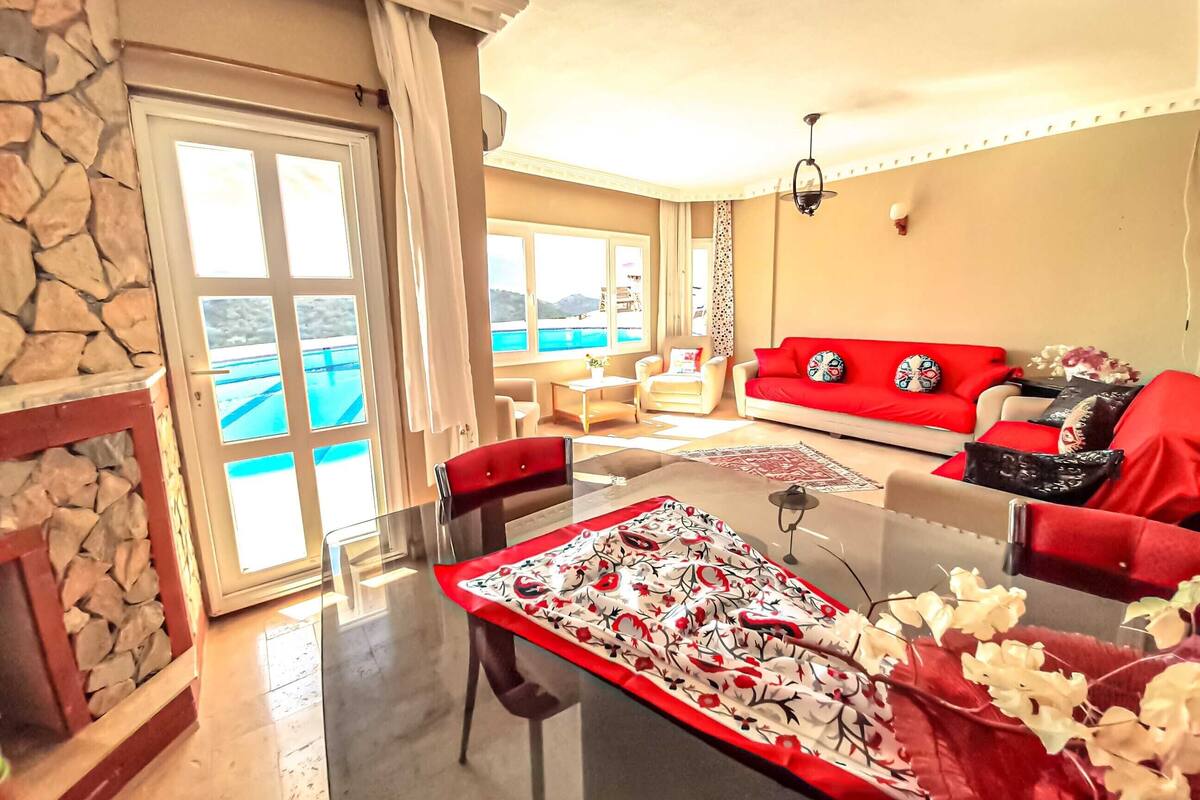 A living room with a red sofa, a glass dining table, and a stone wall.