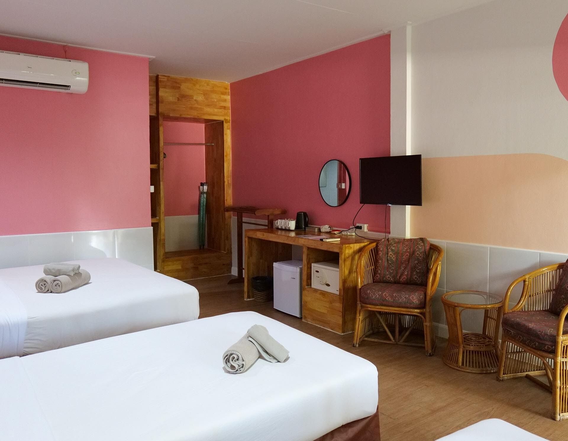 A hotel room with two beds, a desk with a computer, a TV, and wicker furniture.