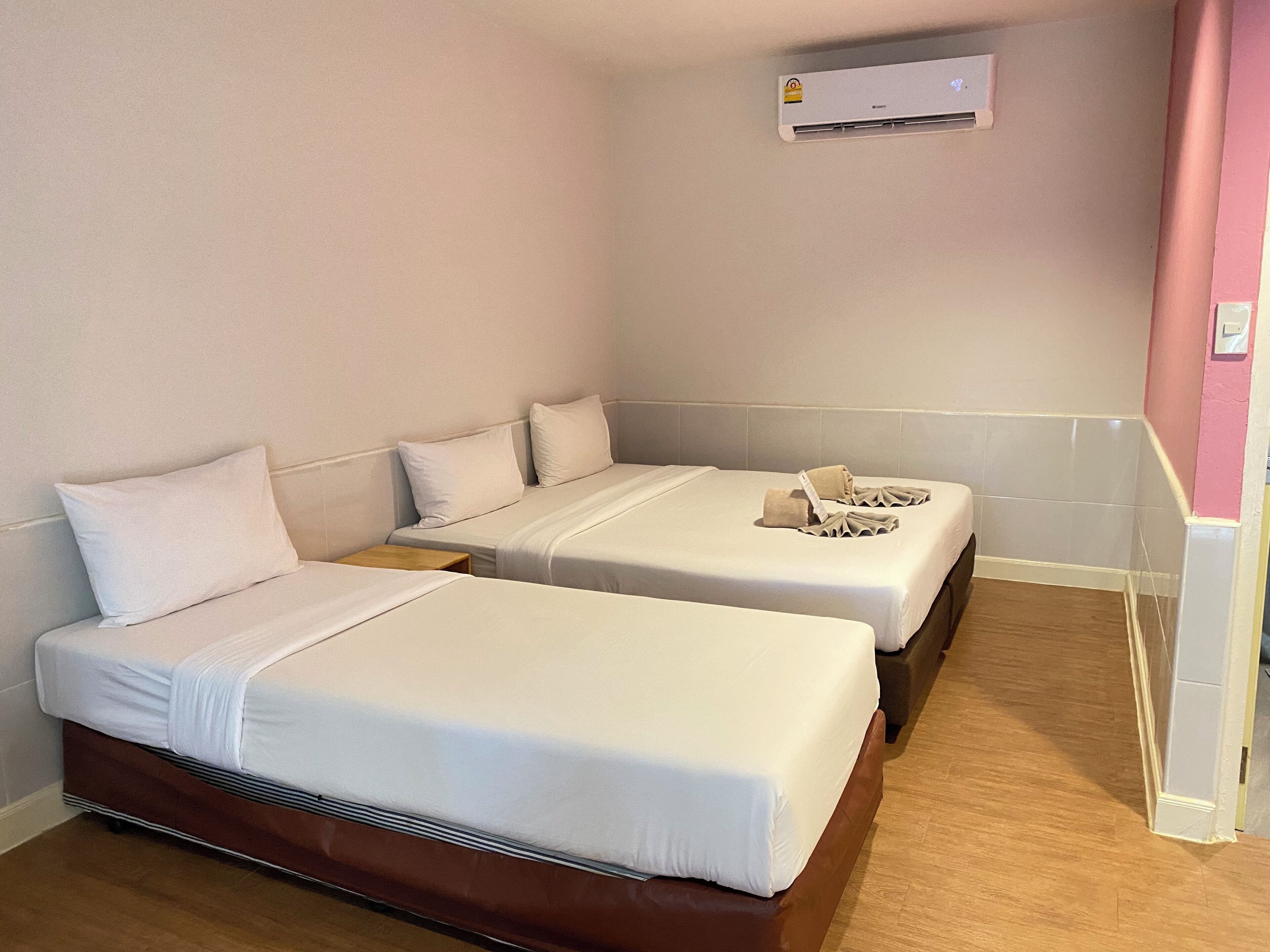 Habitación de hotel con dos camas, piso de madera, aire acondicionado de pared y una mesita de noche pequeña.