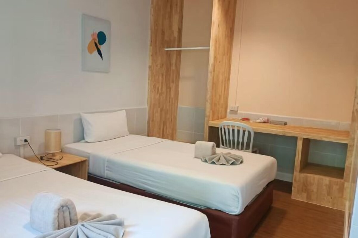 Una habitación de hotel con dos camas individuales, un escritorio de madera, una silla y una mesita.
