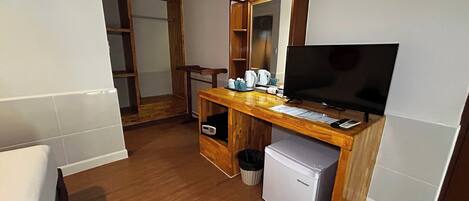 A compact hotel room with a wooden desk, a television, a small refrigerator, and a mirror above the desk.