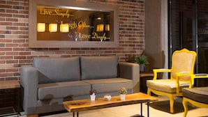 A cozy seating area with a grey sofa, a wooden coffee table, and two yellow chairs with patterned cushions. A mirror with inspirational phrases is mounted on the brick wall. - Sun Suit Hotel (Izmir)