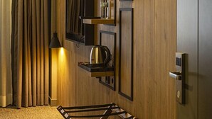 A hotel room with a wooden wall, a TV mounted on it, a kettle, a small shelf with items, a lamp, and a bed frame. - Sun Suit Hotel (Izmir)