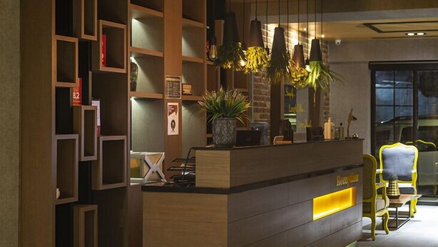 A reception desk with a wooden finish, pendant lighting, and a potted plant. - Sun Suit Hotel (Izmir)