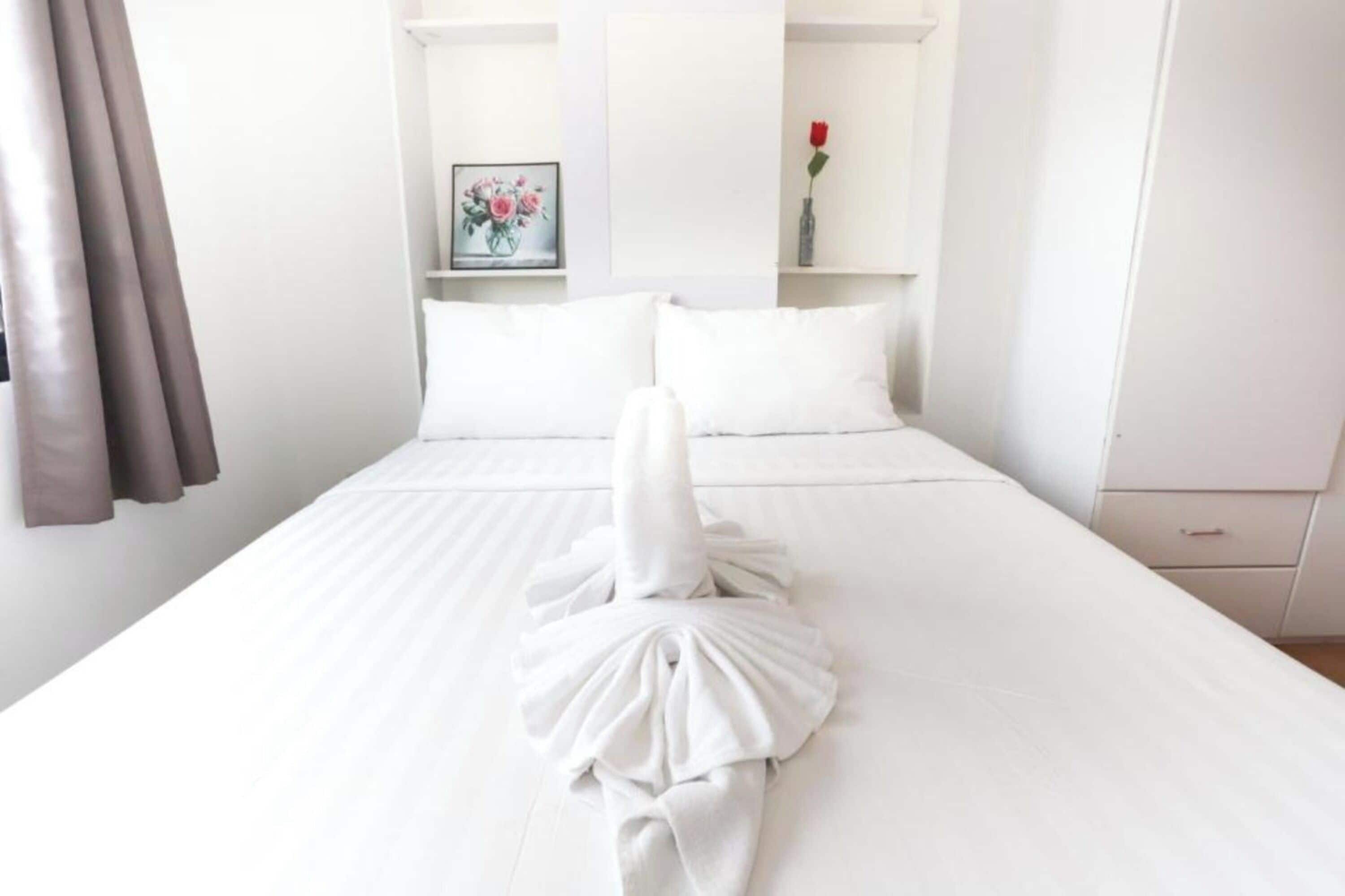A hotel room with a neatly made bed, a framed picture on the wall, and a vase with a single red rose.