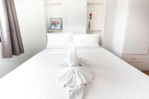 A hotel room with a neatly made bed, a framed picture on the wall, and a vase with a single red rose. - C Tower Hotel (Surat Thani)