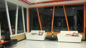 A modern living room with two white sofas, a small table, and large windows with orange frames. - C Tower Hotel (Surat Thani)
