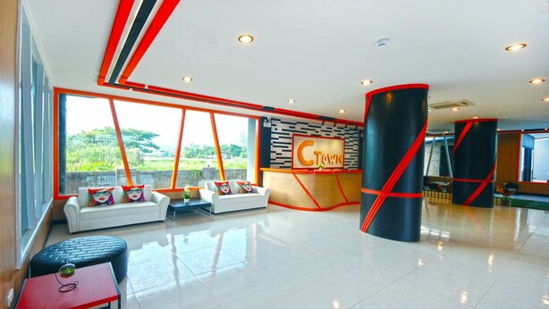 A modern lobby with a reception desk, seating area, and large windows offering a view of greenery. - C Tower Hotel (Surat Thani)