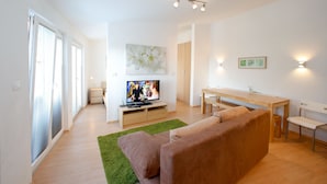 Una sala de estar moderna con un sofá, un televisor, una mesa de comedor de madera y una alfombra verde.