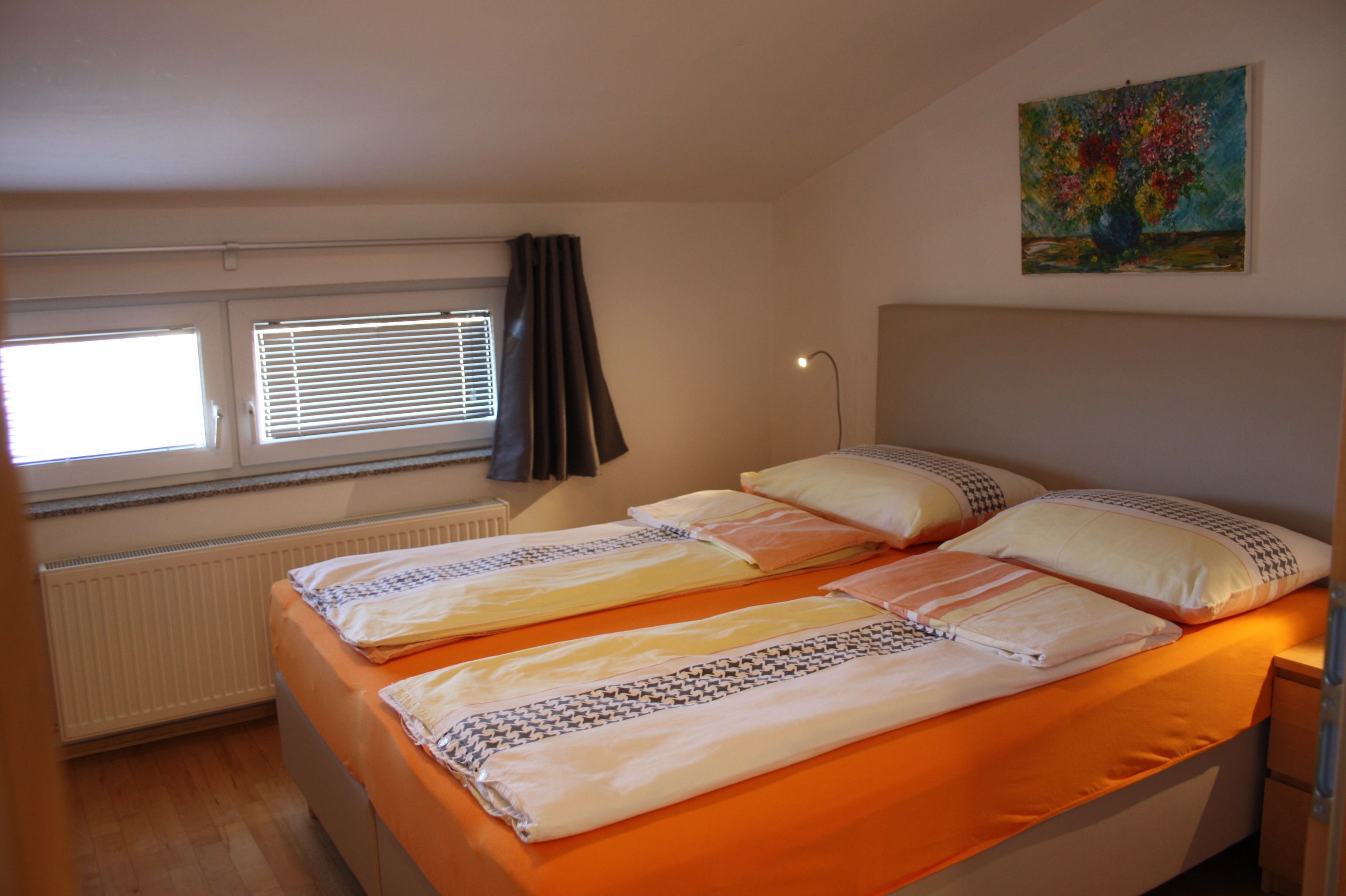 A room with two beds, a radiator, a window with blinds, and a painting on the wall.