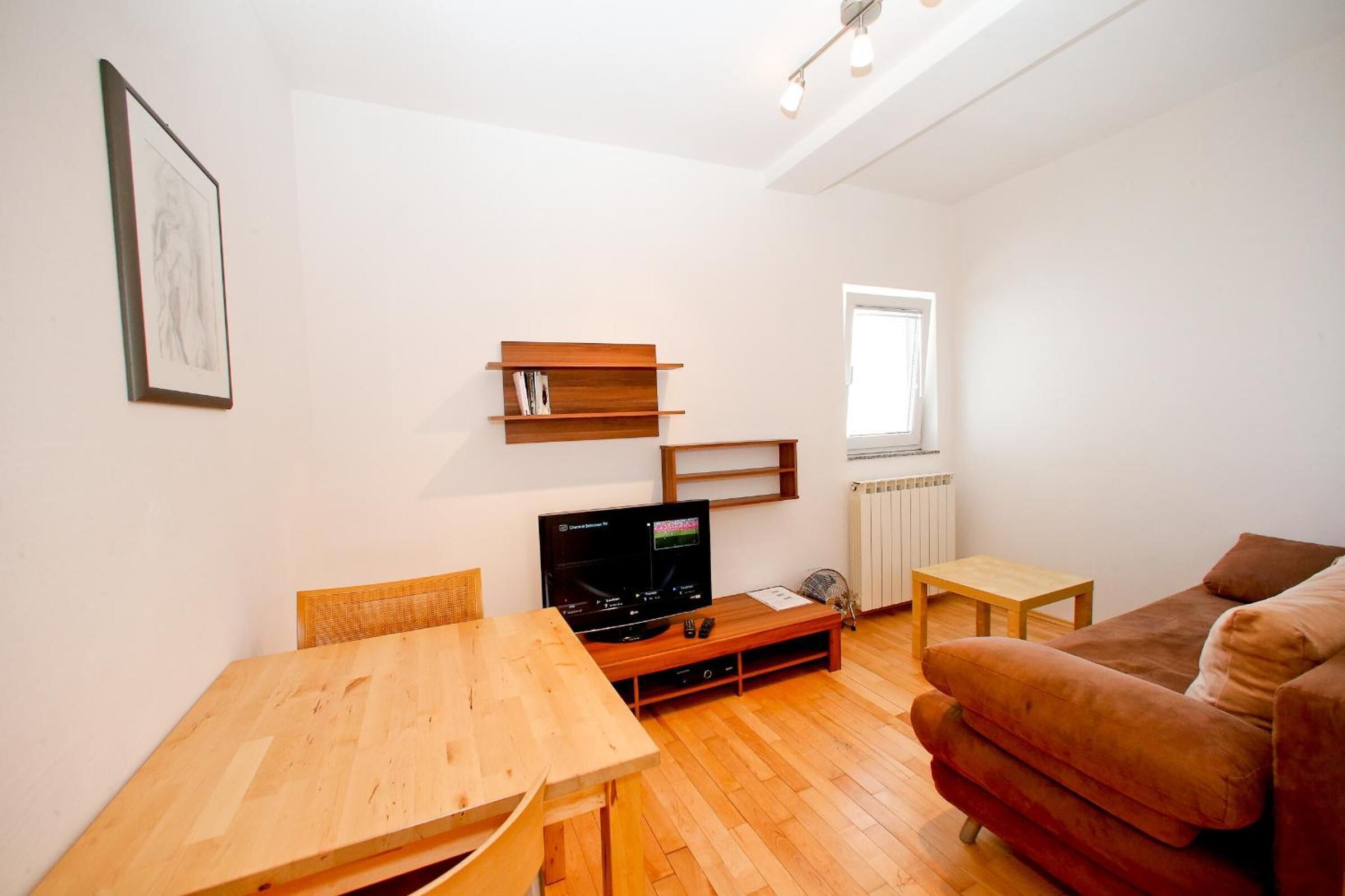 A modern living room with a wooden table, a brown sofa, a TV, and a bookshelf.