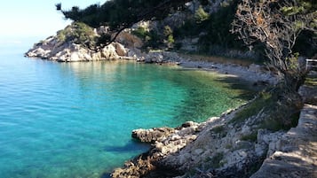 A coastal landscape with clear turquoise water, rocky terrain, and sparse vegetation.