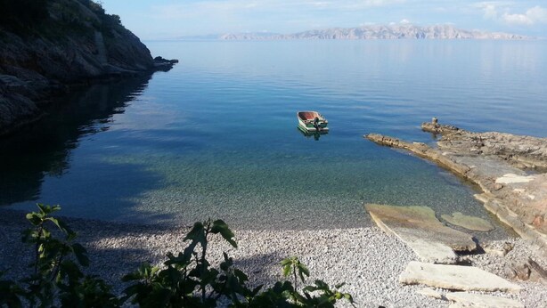 Un lago tranquilo con un pequeño bote anclado cerca de la orilla, rodeado de terreno rocoso y cielos despejados.