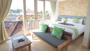 A hotel room with a bed, a bench, a table, and a balcony with a view of buildings. - Green Studio Apartment (Denpasar)