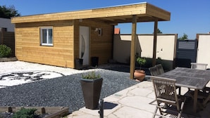 Une cabane en bois dotée d’un patio couvert, d’un espace recouvert de gravier et d’une table avec des chaises.