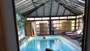 Une piscine intérieure dotée de chaises longues et d’une structure de toit abritée.