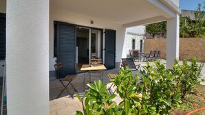 Une terrasse extérieure avec une table et des chaises en bois, une porte-fenêtre coulissante et un mur en pierre.