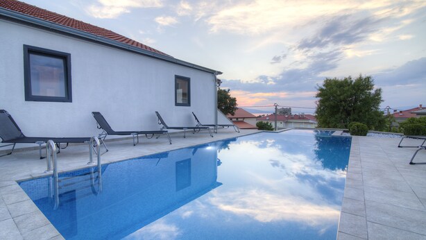 Une piscine avec des chaises longues et un bâtiment blanc doté de fenêtres.