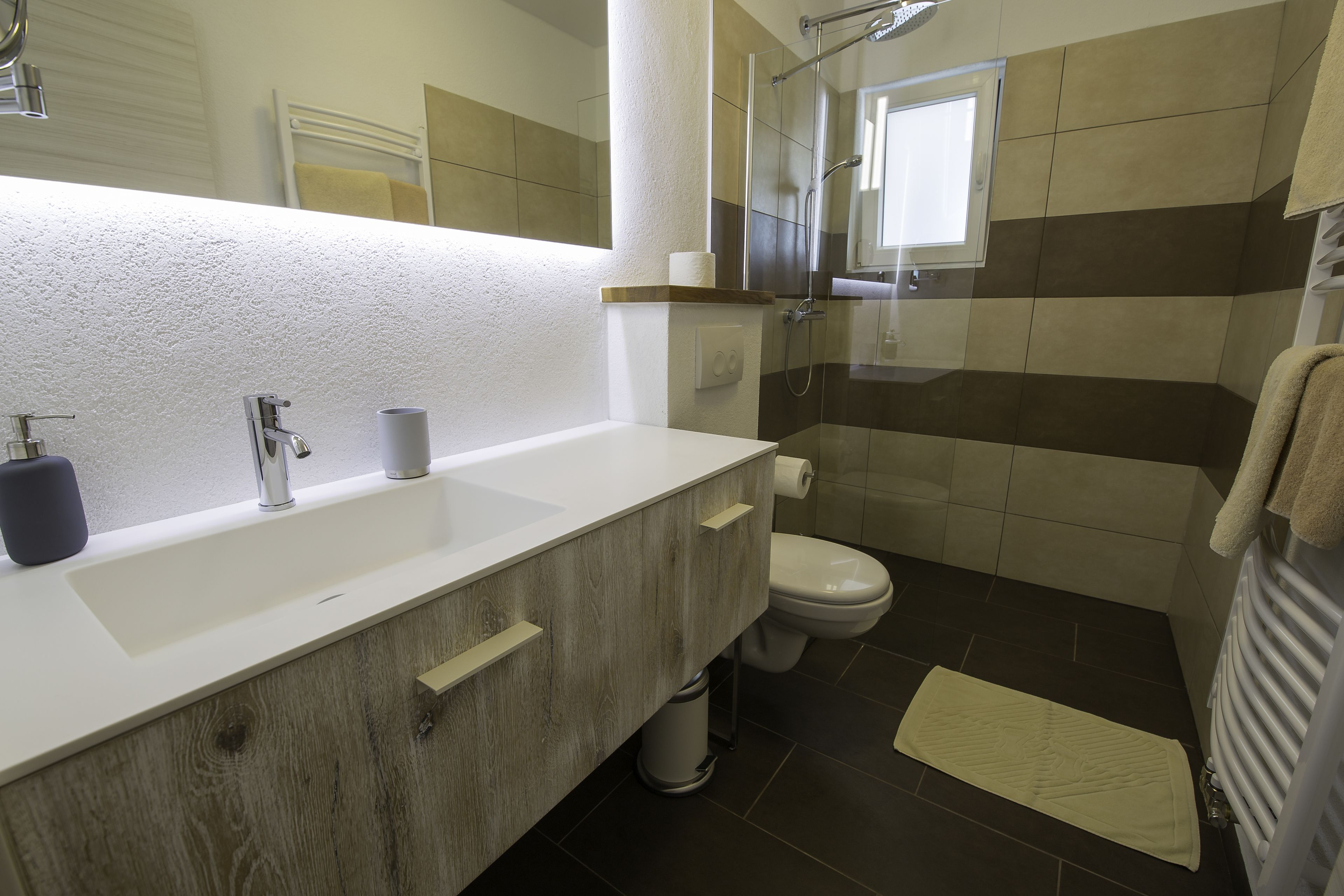 A modern bathroom with a wooden vanity, a white sink, a toilet, and a glass shower enclosure.