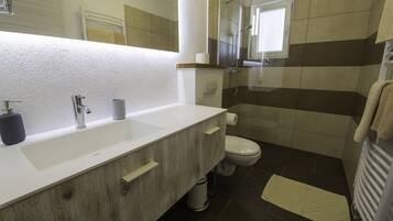 Un baño moderno con tocador de madera, un lavabo blanco, un inodoro y una cabina de ducha con mampara de vidrio.