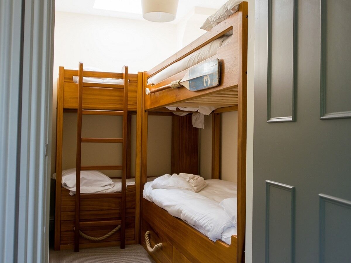 A bunk bed room with a ladder, a small shelf, and a door.