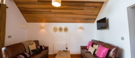 A cozy living room with two brown leather sofas, a wooden coffee table, and a hanging light fixture.