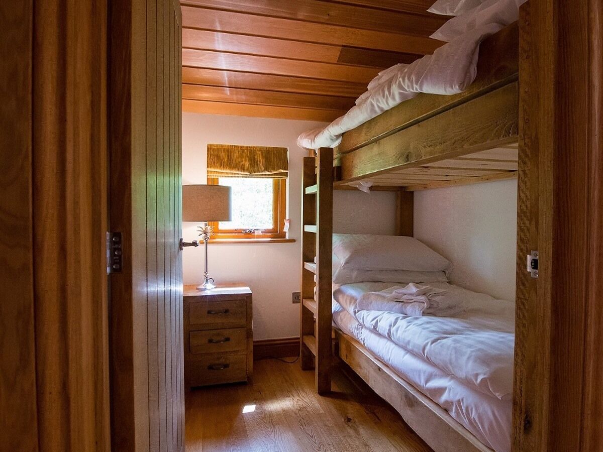 A compact bedroom with a bunk bed, a bedside table with a lamp, and a window with a curtain.
